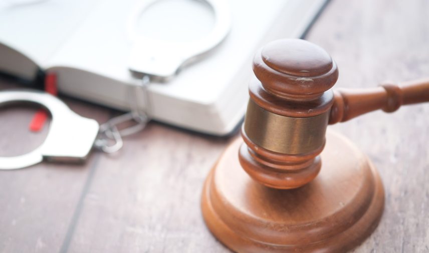 A close-up image of a judicial gavel and handcuffs on an open law book, symbolizing legal justice.